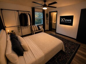 A bedroom with a bed, a ceiling fan, a window with curtains, a wall-mounted TV, and a sign that reads 'X7 STAYS'. - Georgetown Cozy Cottage (Georgetown)
