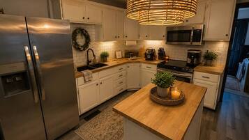 A modern kitchen with a stainless steel refrigerator, a microwave, and a built-in oven. There is a wooden island with a potted plant and a candle.