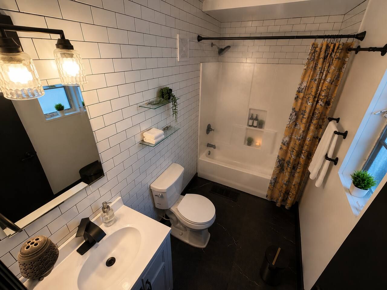 Een moderne badkamer met een wit toilet, een badkuip en een douche. Twee wandlampen, een spiegel en een plank met planten.
