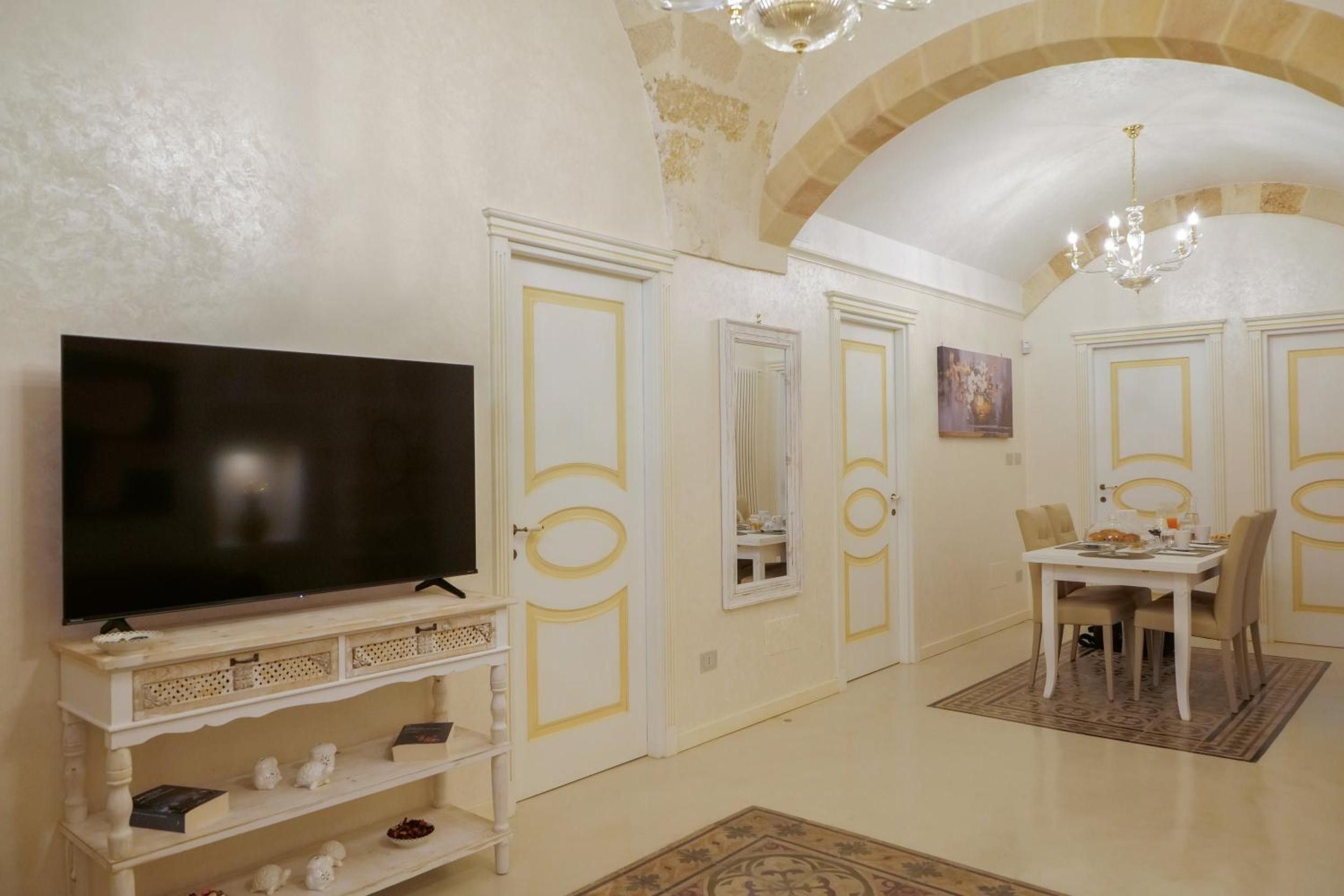 Una habitación con una televisión sobre un mueble, una mesa de comedor con sillas y una araña.