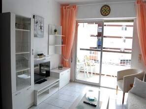 A modern living room with a glass door leading to an outdoor balcony, a flat-screen TV, and a sofa. - One-bedroom Apartment in Nerja (Nerja)