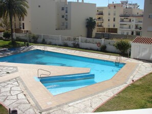 A rectangular swimming pool with a tiled deck, surrounded by a low white wall and a palm tree. - One-bedroom Apartment in Nerja (Nerja)