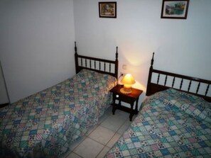 A room with two beds, each with a patterned bedspread, a bedside table with a lamp, and a wall-mounted picture. - One-bedroom Apartment in Nerja (Nerja)