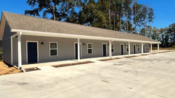 A row of single-story motel rooms with individual doors and windows, a covered parking area, and a clear sky.