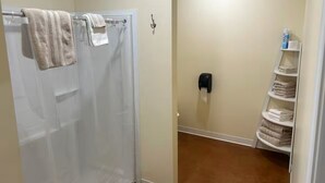 Un baño con ducha, toallero, dispensador de jabón y repisa con toallas dobladas.