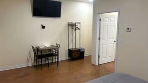 Una habitación con una cama, una mesa de comedor con sillas, un televisor montado en la pared y una puerta.