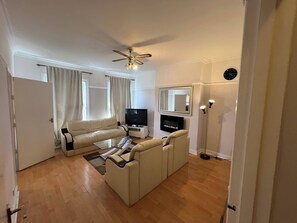 A living room with a sofa, a coffee table, a television, a fireplace, and a ceiling fan. - Apartment Sleeps 6 With Pets Welcome (Croydon)