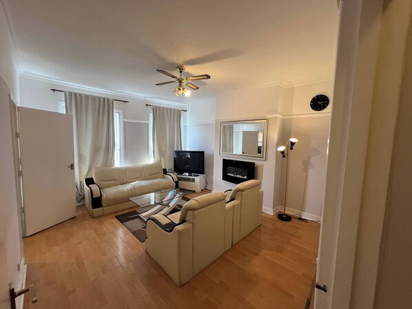 Una sala de estar con un sofá, una mesa de centro, un televisor, una chimenea y un ventilador de techo.