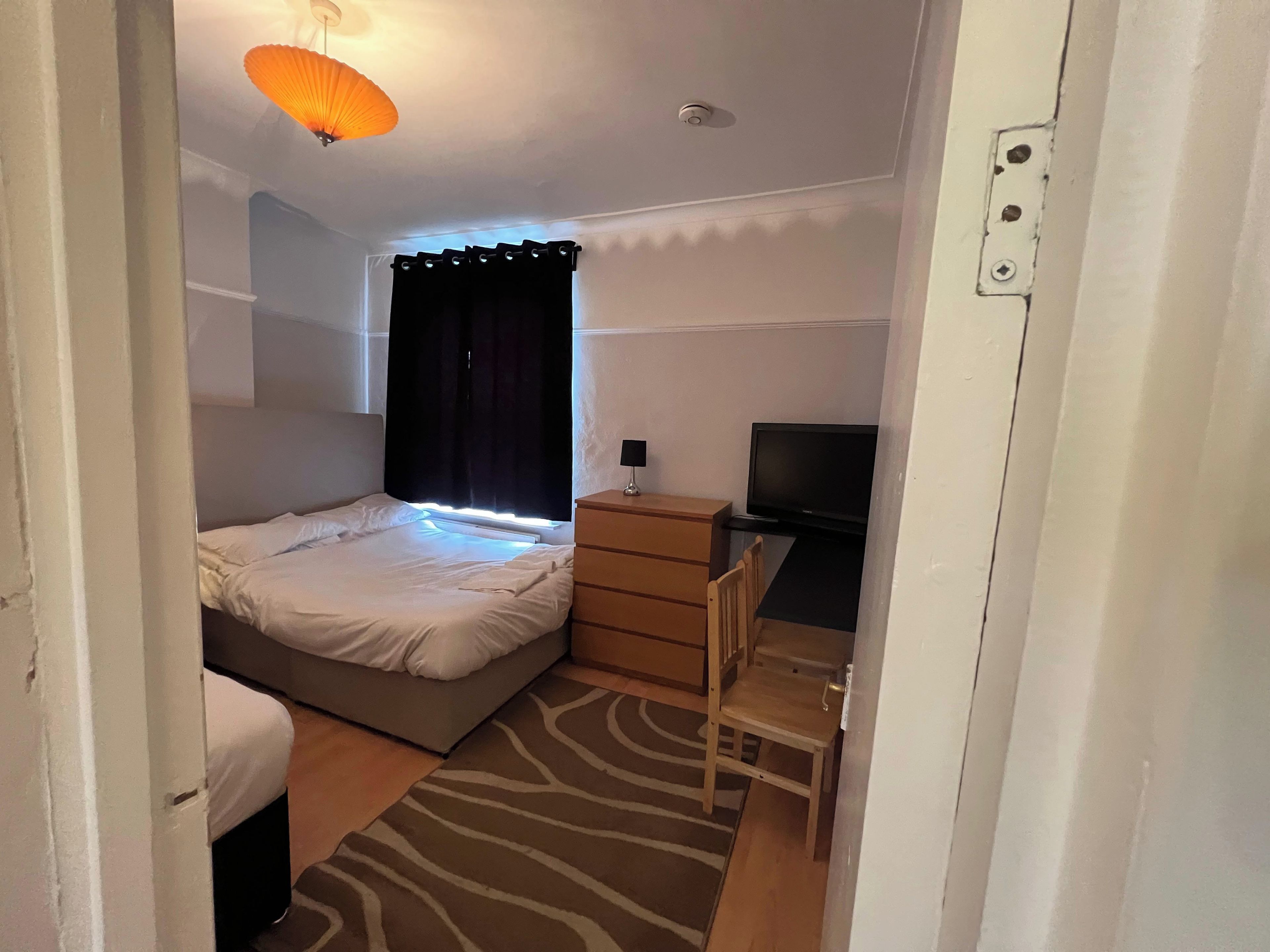 Un dormitorio con cama, escritorio, televisor y ventana con cortinas.