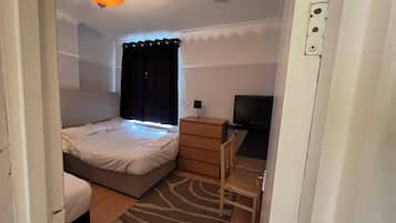 Un dormitorio con cama, escritorio, televisor y ventana con cortinas.