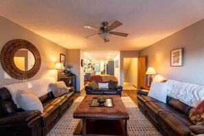 A living room with a ceiling fan, two leather sofas, a coffee table, and a large mirror on the wall. - The Burrow at Silver Creek | Ski Access, Hot Tub (Snowshoe)