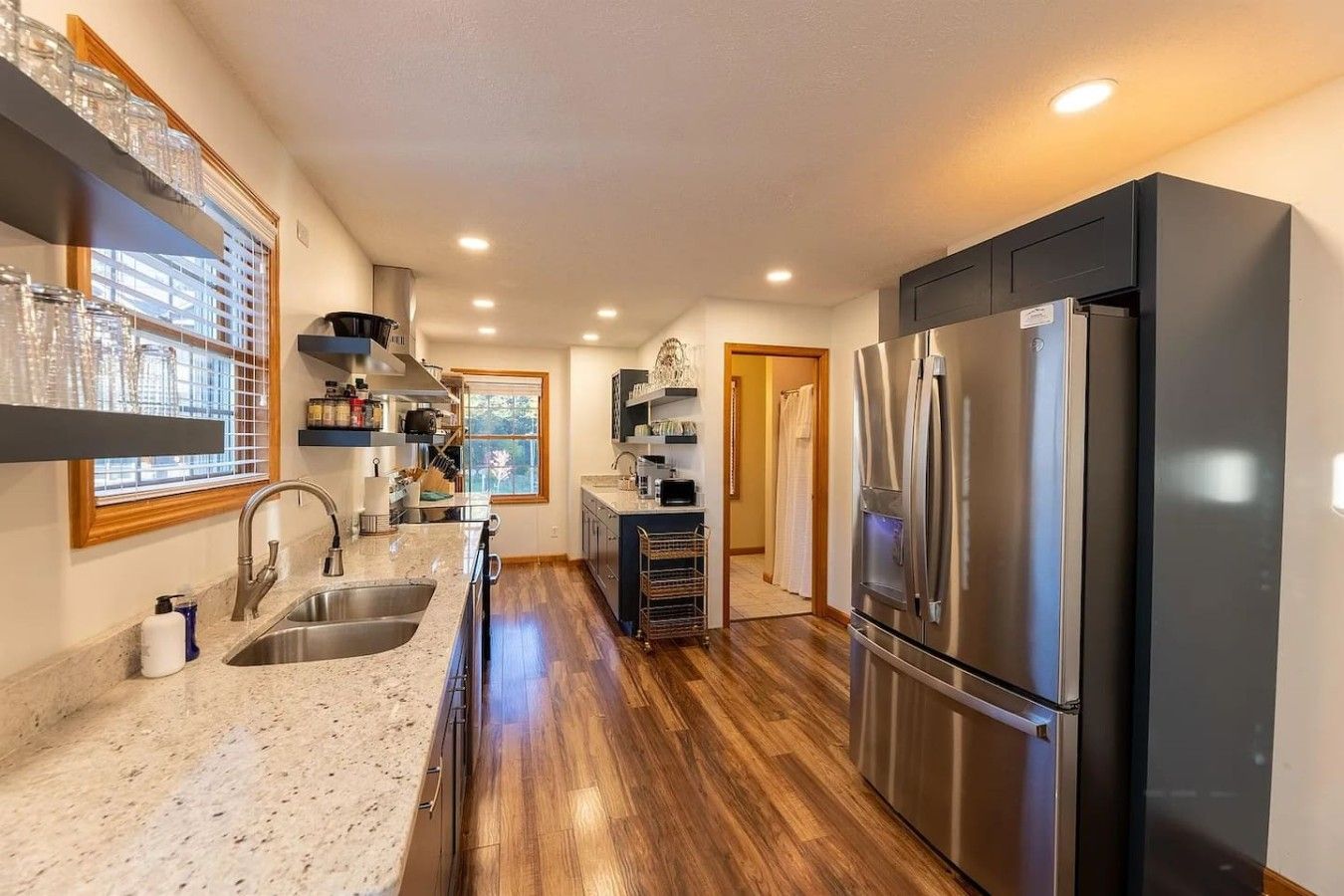 A kitchen with a stainless steel refrigerator, a sink, and wooden flooring.