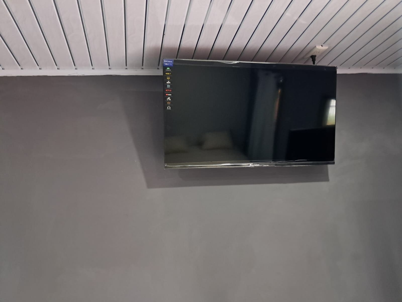 A flat-screen TV mounted on a wall with a control panel on the left.