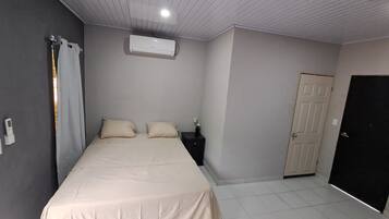 Ein Schlafzimmer mit einem Bett, einem Nachttisch, einer Klimaanlage, einer Tür und einem gefliesten Boden.
