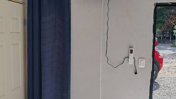 A room with a closed door, a blue curtain, a mounted television, and a power outlet on the wall.