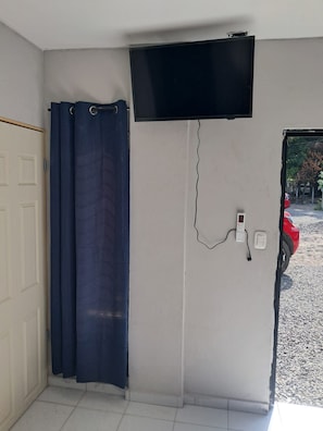 A room with a closed door, a blue curtain, a mounted television, and a power outlet on the wall. - Premium Home  (La Paz Oeste)