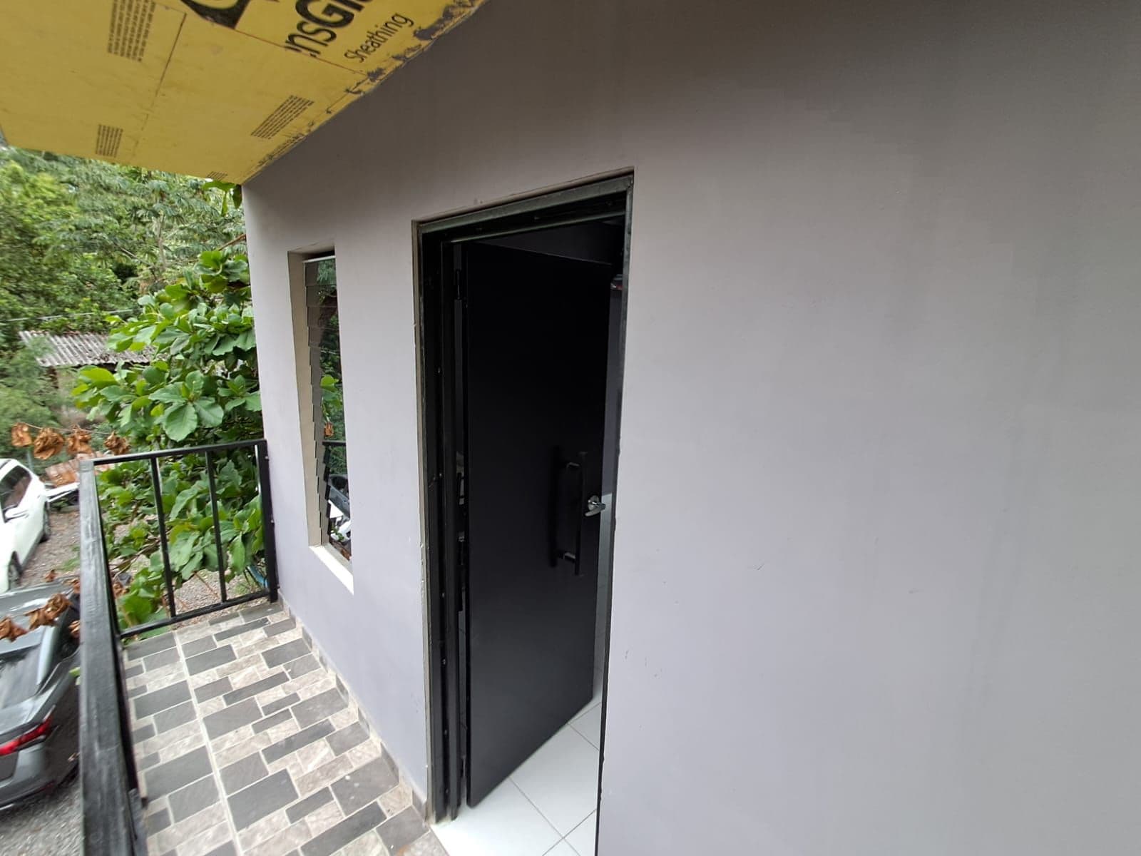 A balcony with a tiled floor, a black door, and a yellow awning.