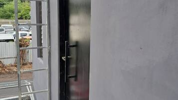 Fachada de un edificio con una escalera metálica, una puerta negra y un estacionamiento al fondo.