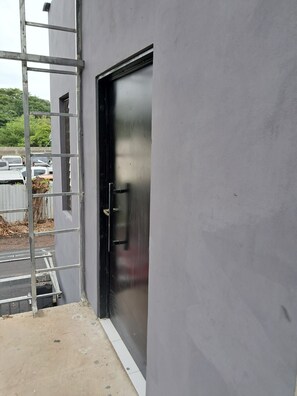 Fachada de un edificio con una escalera metálica, una puerta negra y un estacionamiento al fondo.