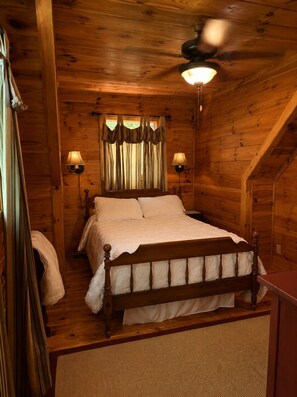 Ein Schlafzimmer einer Holzhütte mit einem Himmelbett, zwei Wandlampen und einem Deckenventilator.