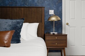 A bedroom with a bed, pillows, a nightstand, a lamp, and a door. - Ruckle Retreat | Hot Tub + Sports Den + Putt Putt (Indianapolis)