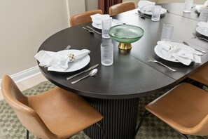 A round dining table with a black surface, surrounded by four brown chairs. - Ruckle Retreat | Hot Tub + Sports Den + Putt Putt (Indianapolis)