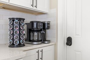 A kitchen with a coffee maker, a coffee pod holder, and a door with a keypad lock. - Ruckle Retreat | Hot Tub + Sports Den + Putt Putt (Indianapolis)