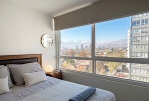 A bedroom with a large window, a bed with pillows, a bedside table with a lamp, and a wall clock. - Domingo Santa Maria by Domus Travels (Santiago)