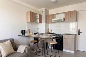 A compact kitchen with a central island, bar stools, a stove, and a built-in oven. - Domingo Santa Maria by Domus Travels (Santiago)