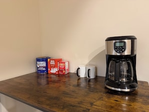 A coffee maker on a wooden table with three boxes of coffee and two white mugs. - Cedar Grove Residence (Surrey)