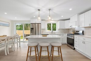 Cocina moderna con armarios blancos, una isla central con taburetes, electrodomésticos de acero inoxidable e iluminación colgante.