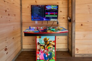A wooden room with a gaming console, a monitor displaying a game menu, and a Mario-themed artwork. - HotTub/Theater/FirePit/GameRoom/5KingSuites! (Sevierville)