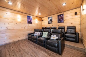 A room with wooden walls and ceiling, featuring a row of black leather reclining chairs with pillows, including one with 'love us' text. - HotTub/Theater/FirePit/GameRoom/5KingSuites! (Sevierville)