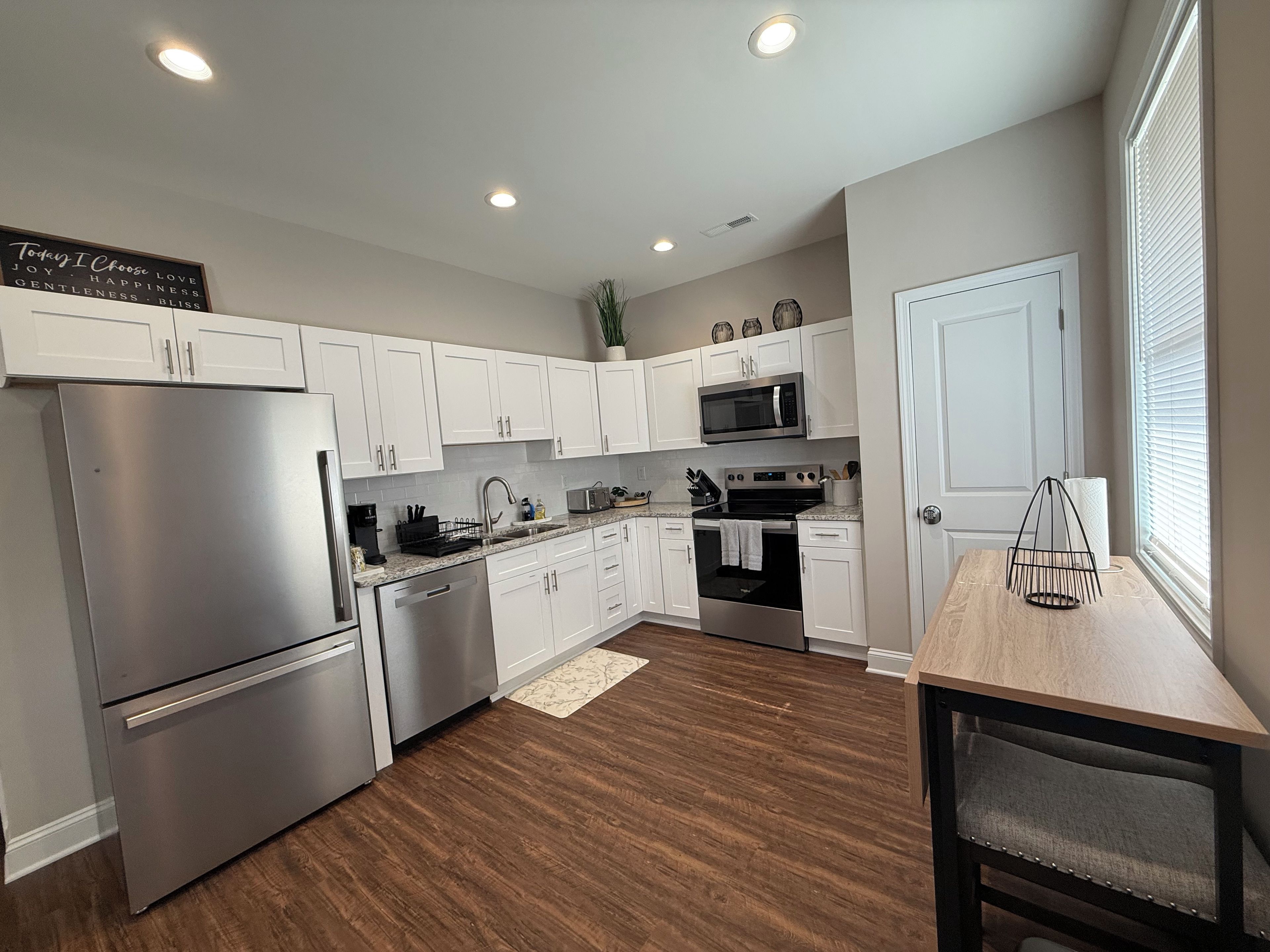A modern kitchen with white cabinets, stainless steel appliances, and a wooden dining table.