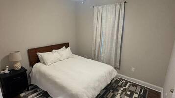 A bedroom with a bed, a nightstand, a ceiling fan, and a patterned rug.