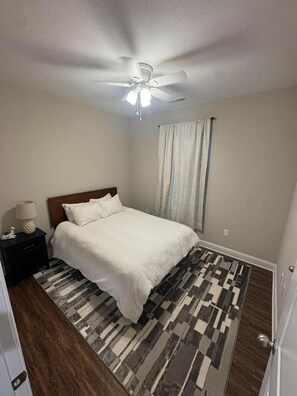 Un dormitorio con cama, mesita de noche, ventilador de techo y alfombra estampada.