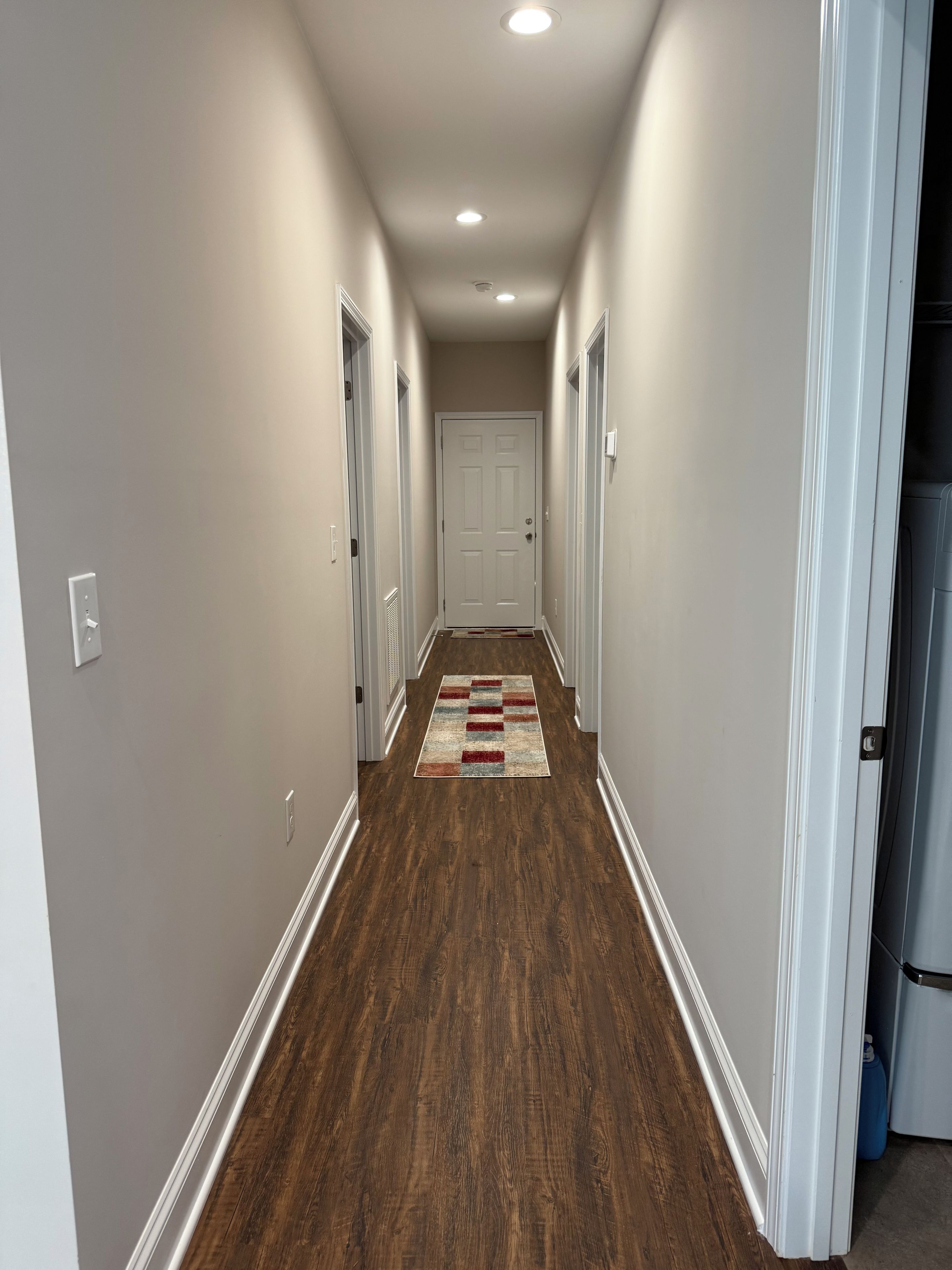 A hallway with wooden flooring, white walls, and a door at the end.