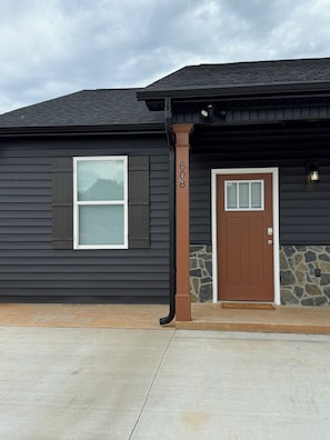 A residential building with a dark exterior, a brown door, and a window with blinds.