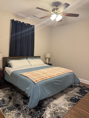 A bedroom with a bed, a ceiling fan, a nightstand, a lamp, and a patterned rug.