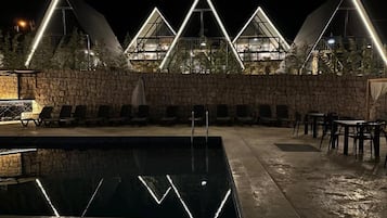 A swimming pool with lounge chairs and tables, surrounded by a stone wall and triangular light structures.