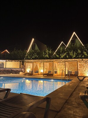 A nighttime pool area with lounge chairs and a stone wall.