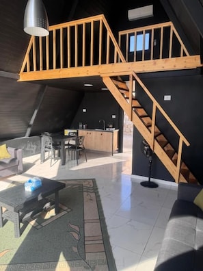 A loft-style living area with a wooden staircase, a kitchen, and a seating area with a sofa and a coffee table.