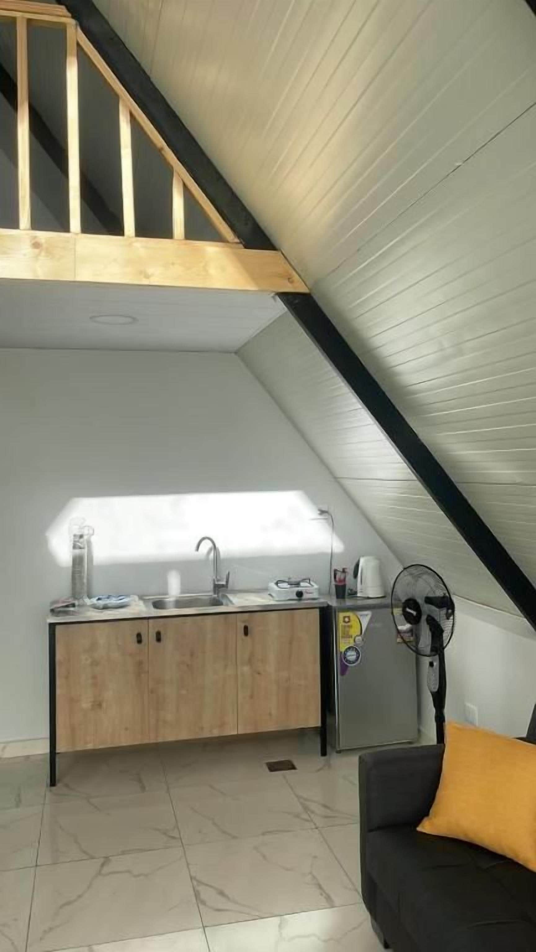 A compact kitchen with a wooden countertop and a built-in sink, a small refrigerator, and a fan.