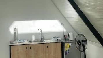 A compact kitchen with a wooden countertop and a built-in sink, a small refrigerator, and a fan.