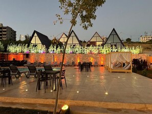 Un patio al aire libre con mobiliario y una piscina, rodeado por un muro de piedra y una fila de edificios con techos triangulares.