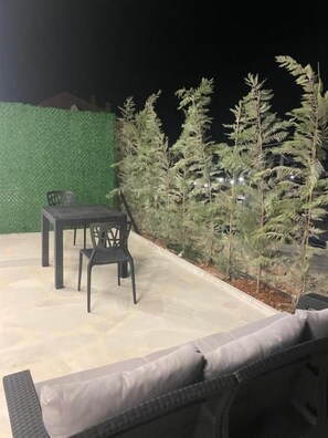 An outdoor seating area with a table and chairs, surrounded by greenery.