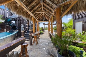 An outdoor bar area with a thatched roof, wooden stools, and a pool table. - The Crab Shack Studio Cabin (Bay City)