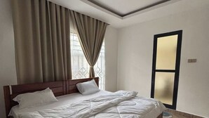 Un dormitorio con una cama de madera, un ventanal con cortinas y una puerta con espejo.