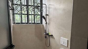 Un baño pequeño con azulejos, que incluye un inodoro, una ducha y una ventana con barrotes.