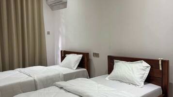 Habitación de hotel con dos camas individuales, cabecera de madera, cortina color beige y aire acondicionado instalado en la pared.